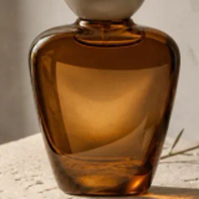 Amber perfume bottle with a curved glass edge on a textured stone surface · Interpolation display
